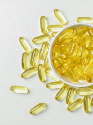 High-angle shot of omega-3 fish oil capsules in a ceramic bowl on a white background.
