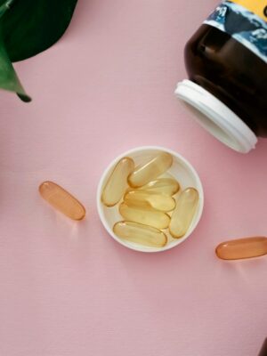 Top view of cod liver oil capsules in a bottle cap on a pink background.